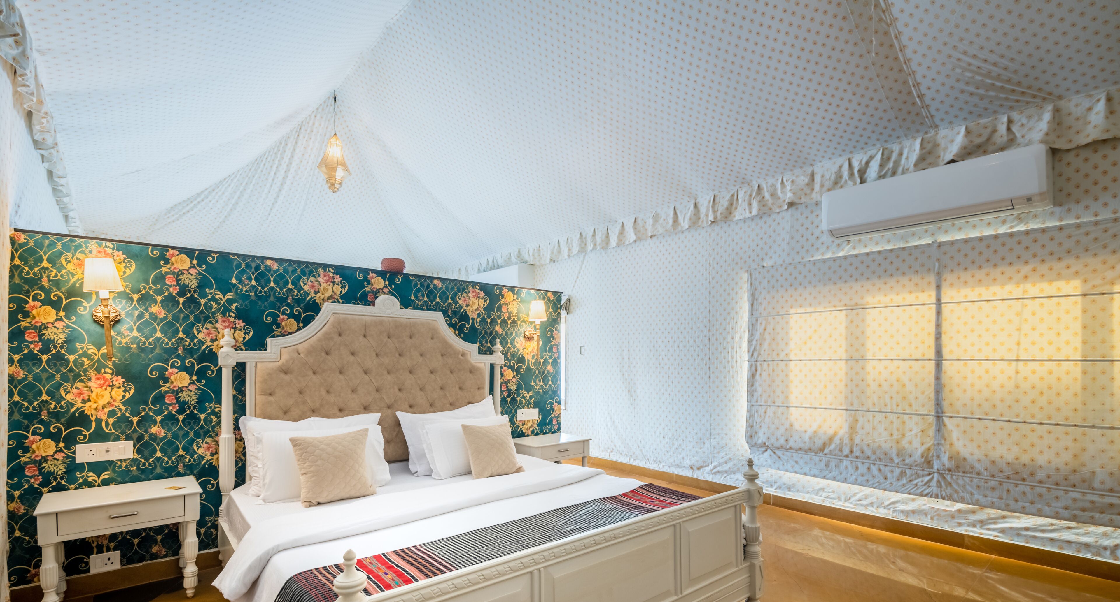 Un dormitorio con una cama grande, una mesita de noche, una pared con papel tapiz floral y una ventana con cortina.