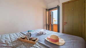 Una cama bien tendida con un atril de madera que sostiene una cafetera, tazas, un sombrero de paja y un cojín sobre una manta con textura.