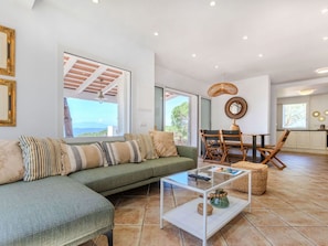 A modern living room with a green sofa, a glass coffee table, and a dining area with wooden chairs.