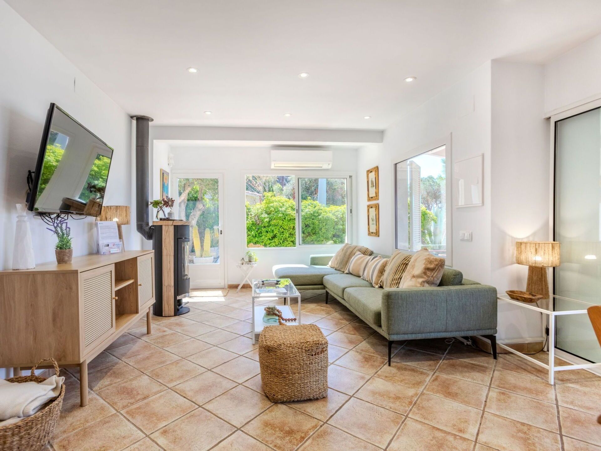 Ein modernes Wohnzimmer mit Fernseher, Sofa, Couchtisch und Blick auf Grünfläche im Freien.