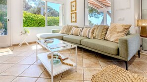 A modern living room with a sofa, coffee table, and a view of greenery outside. - Stunning private villa for 6 guests with WIFI, private pool, A/C, TV and patio (Lloret De Mar)