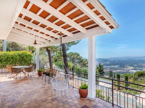 A covered patio with outdoor furniture, a view of the landscape, and a pergola structure.