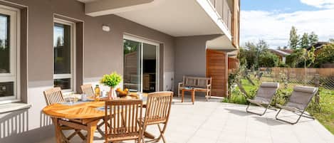 A modern outdoor patio with a wooden table and chairs, a bench, and a small garden area.