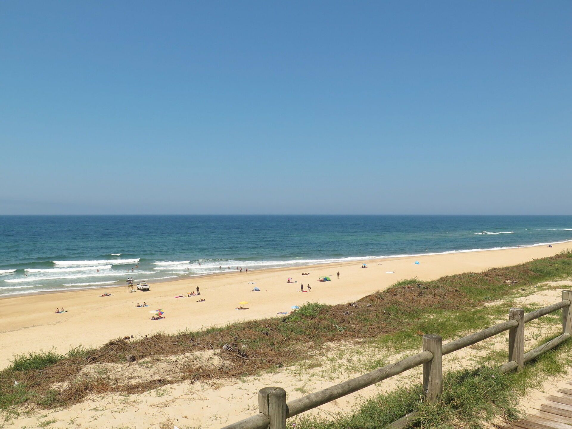 Une plage avec une clôture en bois, un rivage sablonneux et l’océan.