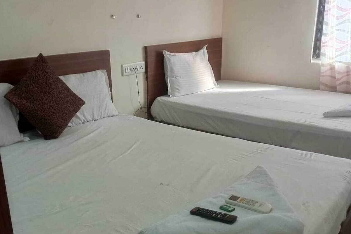 Two single beds with white linens, a brown pillow on the left bed, and a remote control on the right bed.