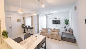 Een moderne woonkamer met een eethoek, een zithoek en een aan de muur bevestigde televisie.