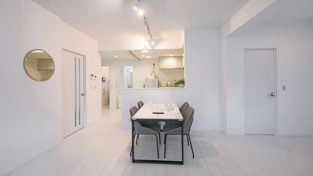 Een moderne, minimalistische eethoek met een witte tafel en stoelen, een ronde spiegel en een hanglamp.