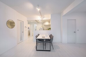 A modern, minimalist dining area with a white table and chairs, a round mirror, and a pendant light. - Miyako Beach Resort (Miyakojima)