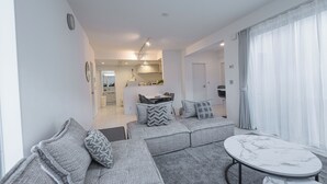 Een moderne woonkamer met een grijze modulaire bank, een marmeren salontafel en uitzicht op de keuken op de achtergrond.