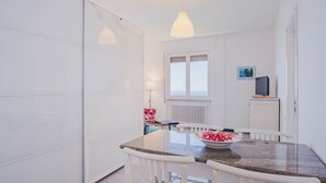 A compact kitchen with white cabinets, a dining table with chairs, a small TV, and a window with a view.