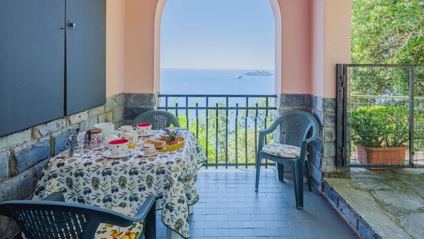 A balcony with a table set for dining, overlooking the sea.