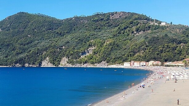 Una playa costera con un mar azul cristalino, orilla de arena y colinas verdes al fondo.