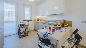 Una cocina moderna con armarios blancos, una mesa de comedor preparada para cuatro personas y vistas de la ciudad a través de amplias ventanas.