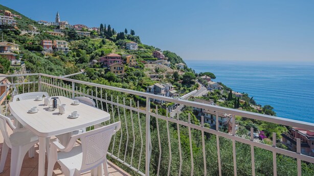A balcony with a table and chairs, overlooking a coastal town with buildings on a hillside and the sea in the background. - Lovely apartment for 4 guests with WIFI, TV and balcony (Moneglia)