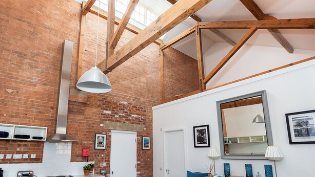 A room with exposed wooden beams, a brick wall, a white door, a large mirror, and a pendant light. - Bowen-Buscarlet at Bicester Heritage (Bicester)
