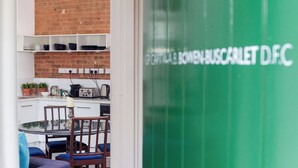 A modern kitchen with white cabinets, a brick wall, and a green glass door with text. - Bowen-Buscarlet at Bicester Heritage (Bicester)