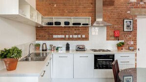 A modern kitchen with white cabinets, a brick wall, and a stainless steel sink. - Bowen-Buscarlet at Bicester Heritage (Bicester)