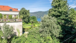 A building with a red roof overlooking a lush green landscape and a lake. - Nice apartment for 4 people with A/C, WIFI, TV and balcony (Porto Valtravaglia)