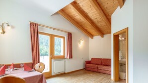 A room with a wooden ceiling, a dining table with chairs, a sofa, and a window with curtains.