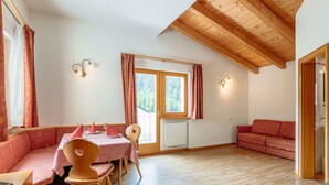A cozy room with a wooden ceiling, a dining table with chairs, a sofa, and a window with curtains.