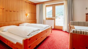 A wooden-paneled room with a bed, a desk, and a view of a mountain.