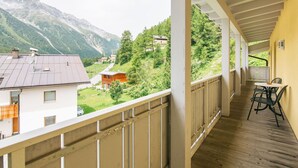 Ein Balkon mit Holzboden, einem Tisch mit Stühlen und Blick auf eine gebirgige Landschaft mit Häusern.