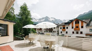 Una terraza con mesas al aire libre, sombrillas blancas y vistas a montañas nevadas.
