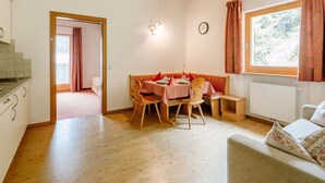 Una habitación acogedora con suelos de madera, una mesa de comedor con sillas, un sofá, una ventana con cortinas y un radiador.