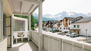 A balcony with a view of a mountain range, a row of houses, and parked cars.