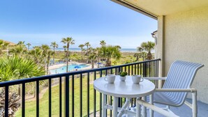 A balcony with a view of a pool and beach, a table with cups and a plant, and a striped chair.