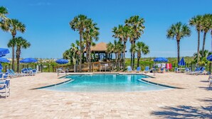 A pool area with lounge chairs and umbrellas, surrounded by palm trees.