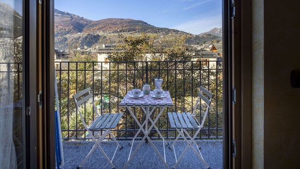 Een balkon met een tafel voor twee, met uitzicht op een bergachtig landschap.
