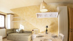 A cozy room with a sofa, dining table set for two, and a hanging light fixture. - Nice apartment for 2 guests with WIFI, TV, balcony and pets allowed (Bormio)