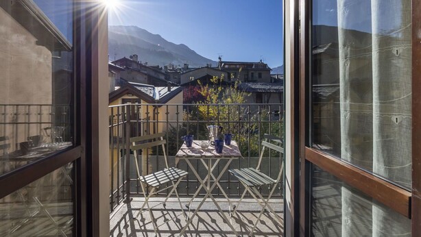 A balcony with a table and chairs, overlooking a mountainous landscape with buildings in the background. - Nice apartment for 2 guests with WIFI, TV, balcony and pets allowed (Bormio)