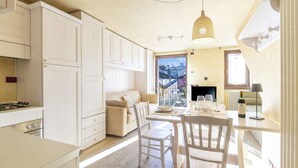 A modern kitchen with white cabinets, a dining area with a table set for two, and a large window with a view of buildings. - Nice apartment for 2 guests with WIFI, TV, balcony and pets allowed (Bormio)