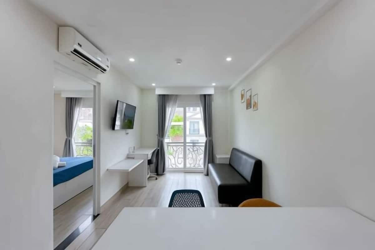 A hotel room with a bed, a desk, a chair, a TV, and a balcony with a railing.