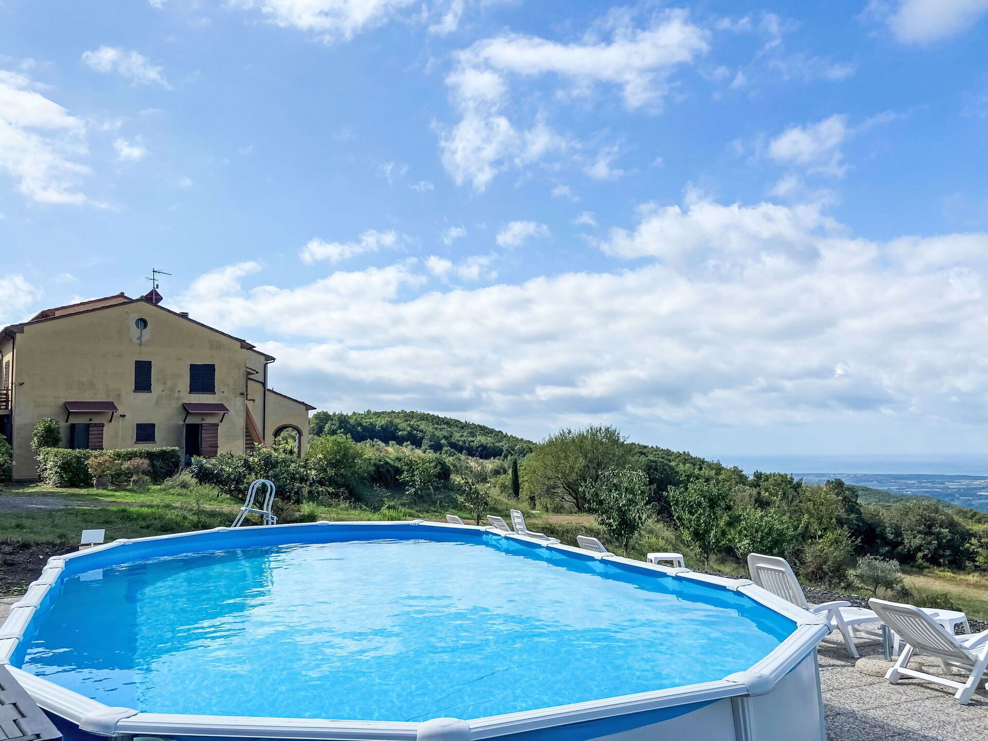 Uma piscina com espreguiçadeiras, uma casa com telhado inclinado e uma paisagem acidentada ao fundo.