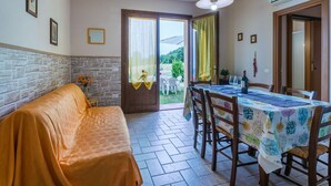 A cozy room with a sofa, a dining table with chairs, a hanging light fixture, and a door leading to an outdoor area. - Beautiful apartment for 7 guests with pool, A/C, WIFI, TV, patio, pets allowed and panoramic view (Castellina Marittima)