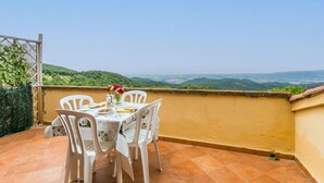 Una terraza con una mesa para dos, rodeada de sillas blancas, con vistas a un paisaje pintoresco.