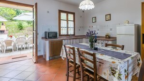 Una cocina con una mesa, sillas, microondas, refrigerador y una ventana con cortinas.
