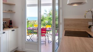 A modern kitchen with a sliding glass door leading to an outdoor dining area with a view of the sea. - Beautiful private villa for 6 guests with private pool, WIFI, TV and terrace (Préfailles)