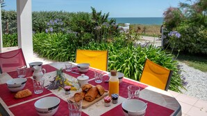 A table set for breakfast with croissants, a bottle of orange juice, and a view of the sea. - Beautiful private villa for 6 guests with private pool, WIFI, TV and terrace (Préfailles)