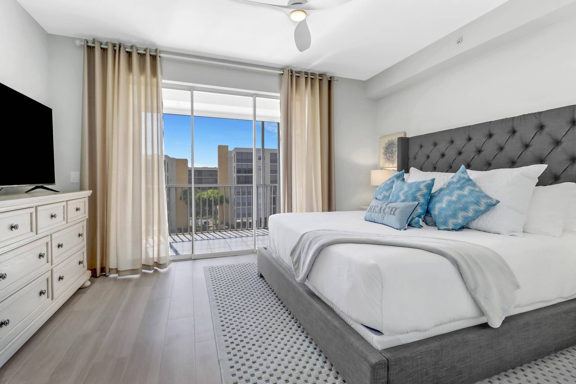 Un dormitorio con una cama grande, un televisor en una cómoda y un balcón con cortinas.