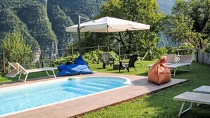 A swimming pool with lounge chairs and a covered area, surrounded by a grassy lawn and mountains in the background. - Stunning private villa with WIFI, private pool, TV, patio, pets allowed and panoramic view (Tione Di Trento)