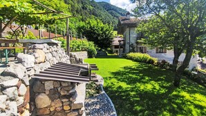 A stone wall with a wooden bench, a well-maintained lawn, and a building with a tiled roof in the background. - Stunning private villa with WIFI, private pool, TV, patio, pets allowed and panoramic view (Tione Di Trento)