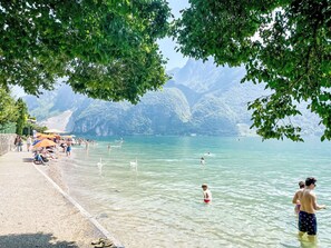 A beach with clear water, people swimming and sunbathing, and mountains in the background.