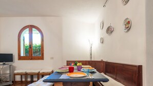 Un coin repas avec un banc en bois, une table ornée d’assiettes colorées et une fenêtre à arc.