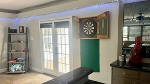 Een kamer met een dartbord, een plank met boeken en een koffieapparaat.