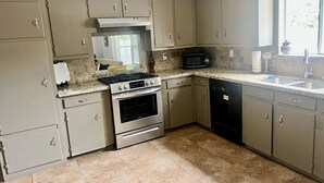 Een keuken met beige kastjes, een gasfornuis, een oven, een magnetron en een vaatwasser.