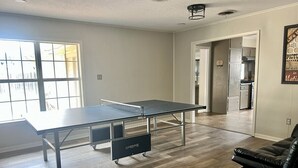 Een kamer met een tafeltennistafel, een zwarte leren bank en een keuken in de achtergrond.